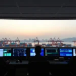 Supply chain managers monitoring global logistics data and cargo ship containers at a port control room during sunset