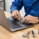 Professional computer repair technician wearing an anti-static wrist strap repairs laptop hardware in a clean, organized workshop equipped with diagnostic tools and spare parts.