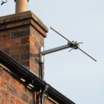 Outdoor TV aerial professionally mounted on house chimney with secure mast and coaxial cable, showing proper installation and weatherproof setup for long lifespan