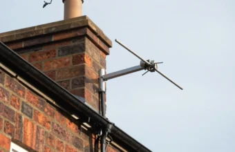 Outdoor TV aerial professionally mounted on house chimney with secure mast and coaxial cable, showing proper installation and weatherproof setup for long lifespan