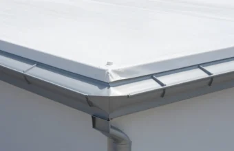 Close-up of a flat roof with a white TPO membrane installed, showing the proper transition and flashing where the roof edge meets a grey aluminum gutter system for effective drainage.