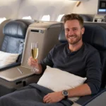 Man enjoying a last minute business class deal to Europe, relaxing in a premium lie-flat seat with a glass of champagne during a flight.