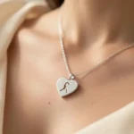 A Lover Girl Necklace featuring a sterling silver heart charm with a feminine figure inside, worn on a delicate chain against a soft cream background.