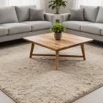 Modern living room with large textured neutral wool area rug anchored under front legs of gray sofa and armchair, featuring natural light and minimalist decor