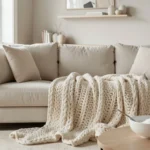 A bright, airy living room featuring a well-maintained light-beige linen sofa with fluffed cushions, a cream throw blanket, and a jute basket, illustrating effective sofa maintenance and home care.
