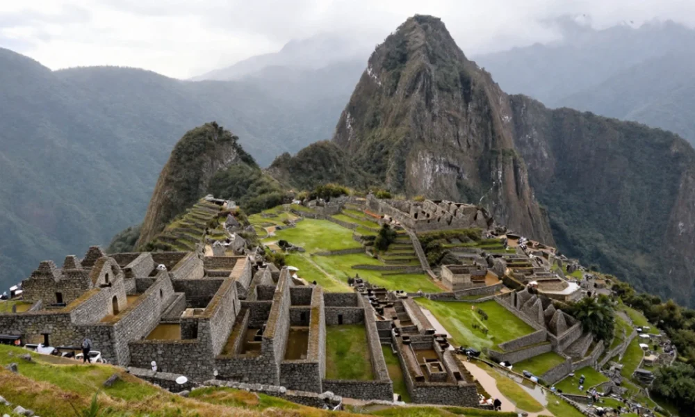 Sunrise panoramic view of Machu Picchu from the Guardhouse viewpoint with Huayna Picchu mountain in the background and visitors walking along the Inca terraces.