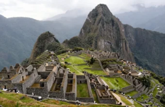 Sunrise panoramic view of Machu Picchu from the Guardhouse viewpoint with Huayna Picchu mountain in the background and visitors walking along the Inca terraces.
